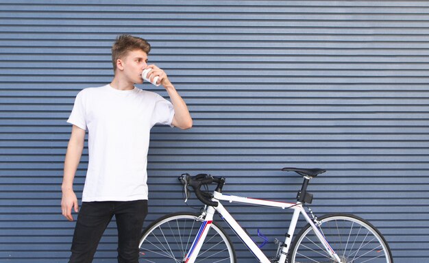 Student, der ein weißes T-Shirt trägt, steht neben einem Fahrrad auf dem Hintergrund einer grauen Wand