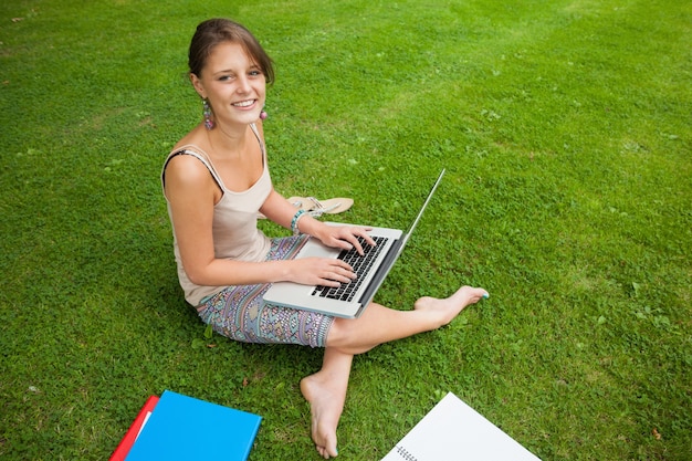 Student, der Laptop mit Büchern am Park verwendet