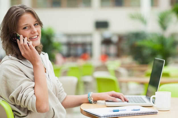 Student, der Mobiltelefon und Laptop am Cafeteriatisch verwendet