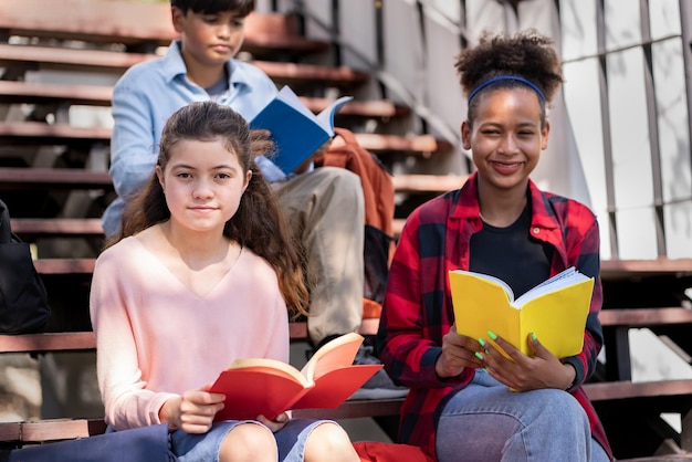 Student hält Buch und schaut mit Freund im Schulpark in die Kamera