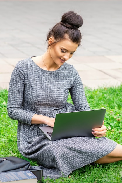 Student junge kaukasische Frau verwendet Laptop, der auf dem Gras auf der Straße sitzt