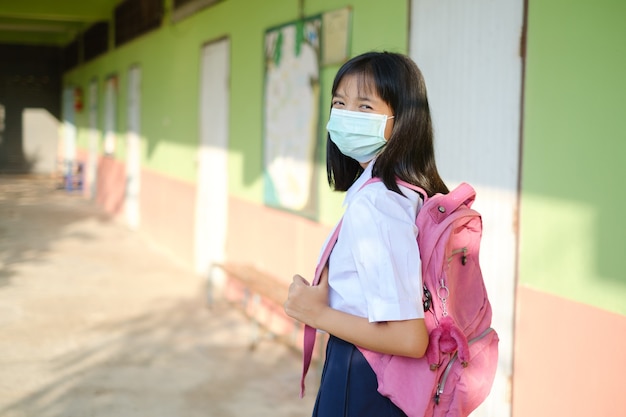 Student Mädchen tragen Maske zu Fuß in der Schule, asiatische Studentin.