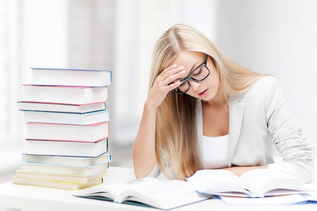 Student mit Stapel Büchern und Notizen, die drinnen lernen