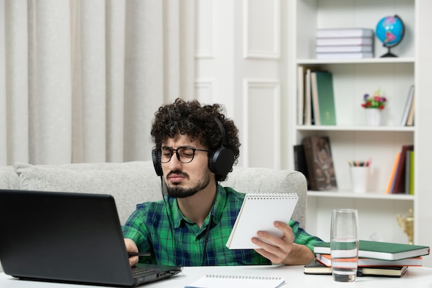 Student online süßer junger Kerl, der am Computer mit Brille im grünen Hemd studiert und auf dem Laptop tippt