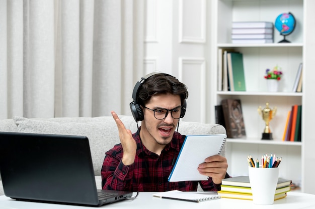 Student online süßer Typ in kariertem Hemd mit Brille, der am Computer studiert, verwirrt über Notizen