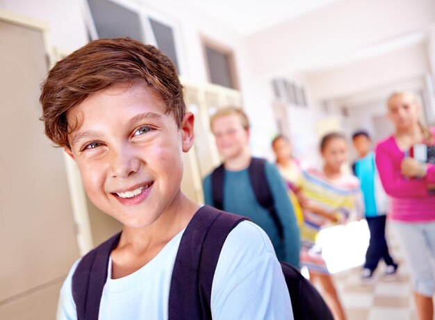 Foto student porträt und junge mit lächeln im flur mit bildung studium und rucksack für die rückkehr zur schule jugend junges kind und lernen mit freunden auf dem campus mit kindern und glücklich aus der klasse und spaß