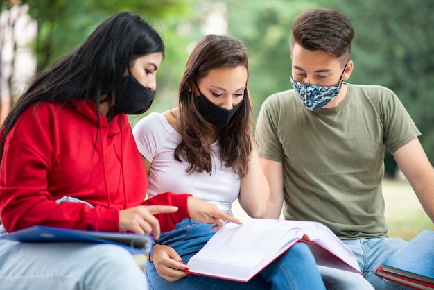 Studenten, die zusammen auf einer Bank im Freien studieren und Covid-Masken tragen