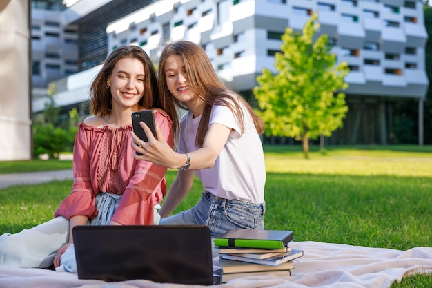Studenten-Selfie in der Natur. Eine Gruppe von College-Freunden macht Selbstporträts auf dem Smartphone und sitzt auf dem Campus