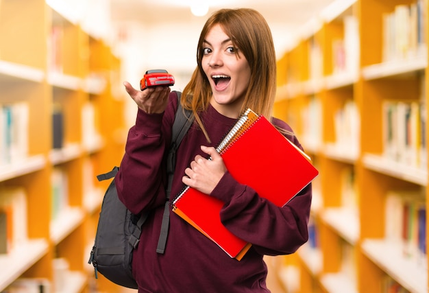 Studentenfrau, die kleines Auto auf unfocused Hintergrund hält. zurück zur Schule