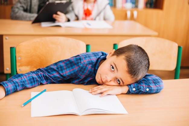 Foto studentenjunge, der auf schreibtisch im klassenzimmer sich lehnt