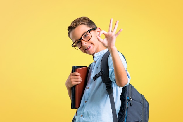 Studentenjunge mit dem Rucksack und Gläsern, die ein okayzeichen mit den Fingern zeigen. zurück zur Schule