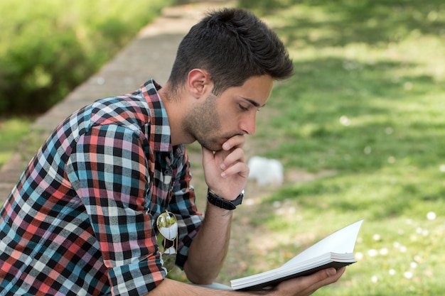 Studentenkerl, der Hausarbeit im Park tut.