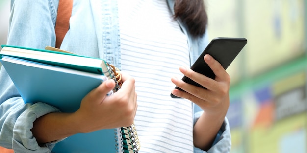 Studentenmädchen, das Bücher hält und Smartphone, Online-Bildung, Technologiekommunikation verwendet