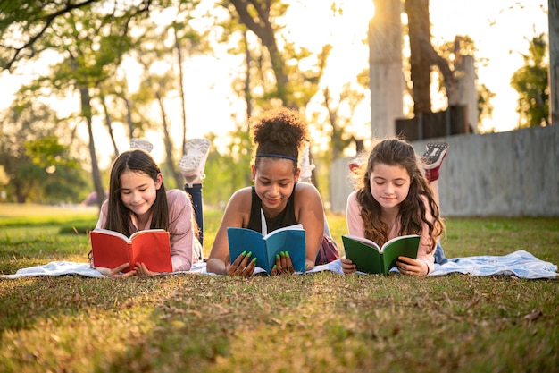 Studentenmädchen legen sich Lesebuch mit Sonnenuntergang im Schulpark hin