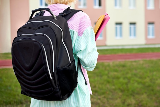 Studentenmädchen mit schwarzem Rucksack und Ordnern für Notizbücher und Bücher in den Händen gehen zur Schule