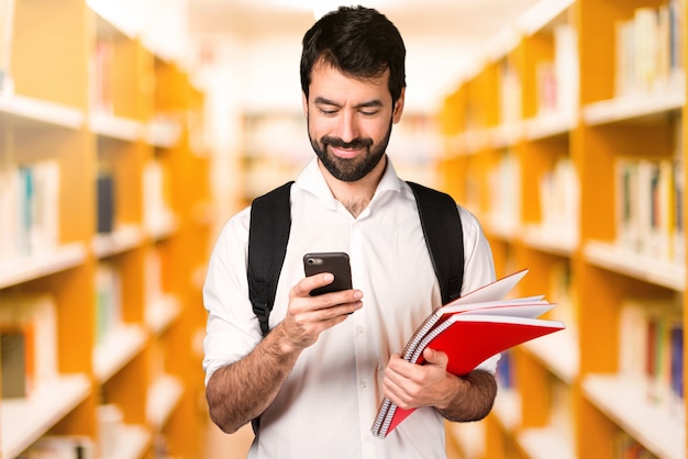 Studentenmann mit Mobile auf defocused Bibliothek