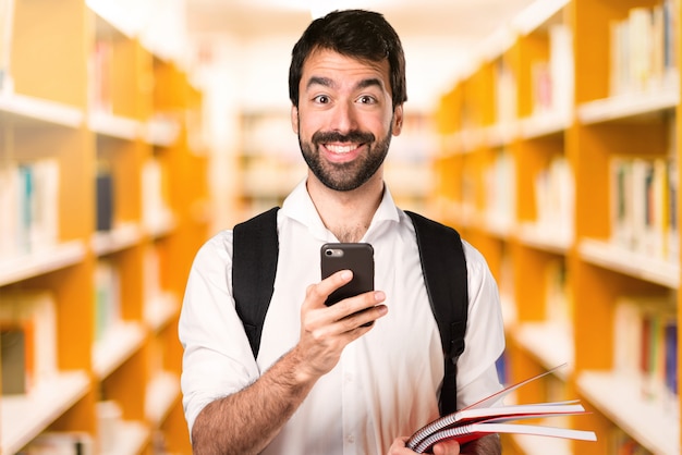 Studentenmann mit Mobile auf defocused Bibliothek
