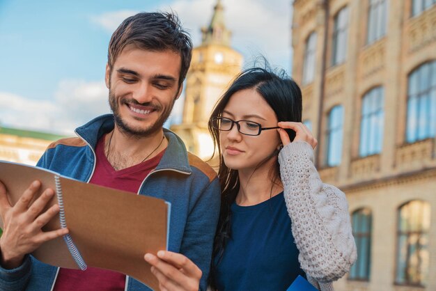 Studentenpaar, das draußen steht und Schreibhefte liest