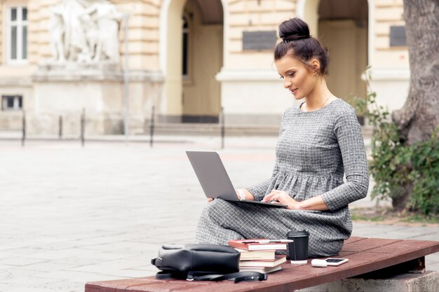 Studentin arbeitet an Laptop auf Bank nahe Universitätsgebäude.