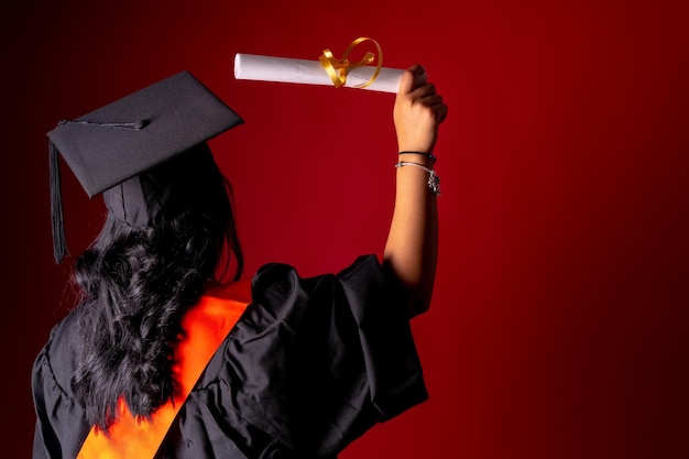 Studentin auf einem Abschlussfoto Abschluss ihrer Ausbildung mit Abschlussdiplom Universitätstunika mit Mütze auf dem Rücken mit Platz für die Kopie des Diploms