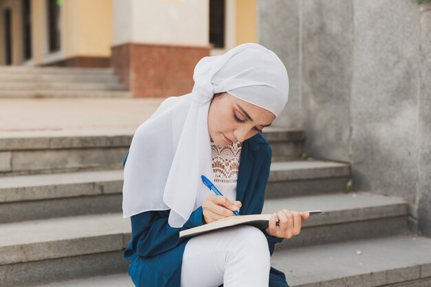 Studentin aus dem Nahen Osten sitzt auf der Treppe in der Bildung und im Wissen des Universitätscampus