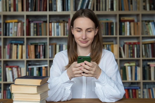 Studentin, die an einem Schreibtisch sitzt und ein Smartphone in der Bibliothek benutzt