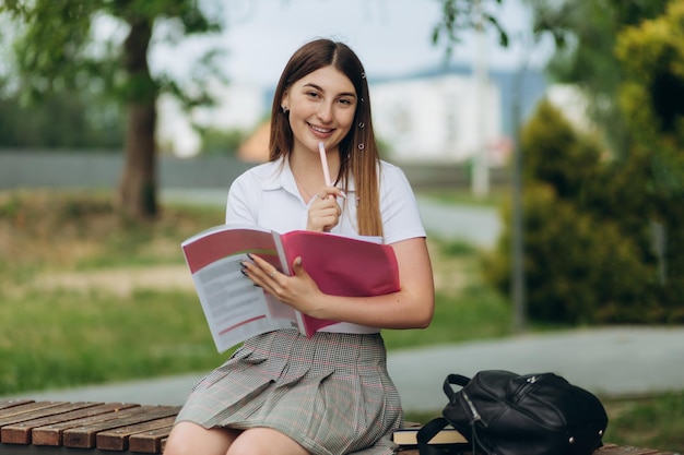 Studentin, die draußen mit Tasche und Buch denkt