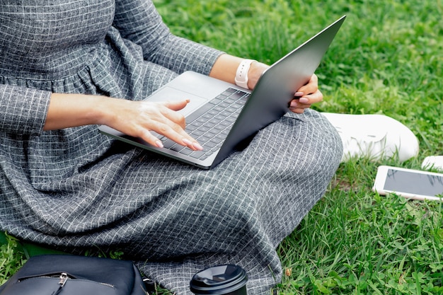 Studentin, die einen Laptop benutzt, während sie auf dem Gras sitzt