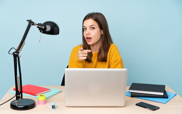 Studentin, die in ihrem Haus an der blauen Wand studiert, überrascht und nach vorne zeigend