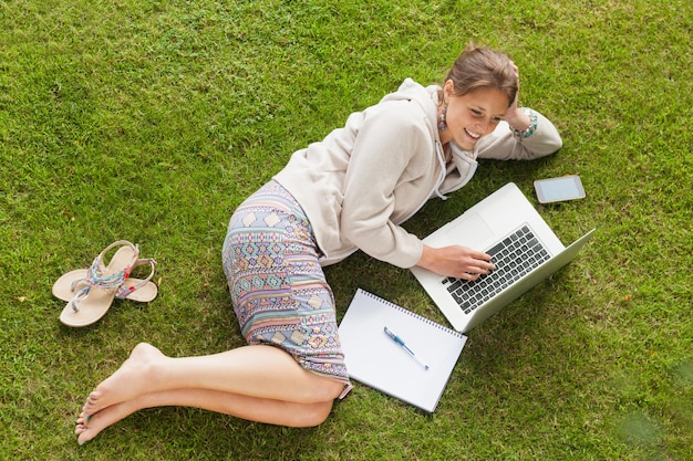 Studentin, die Laptop mit Büchern am Park verwendet