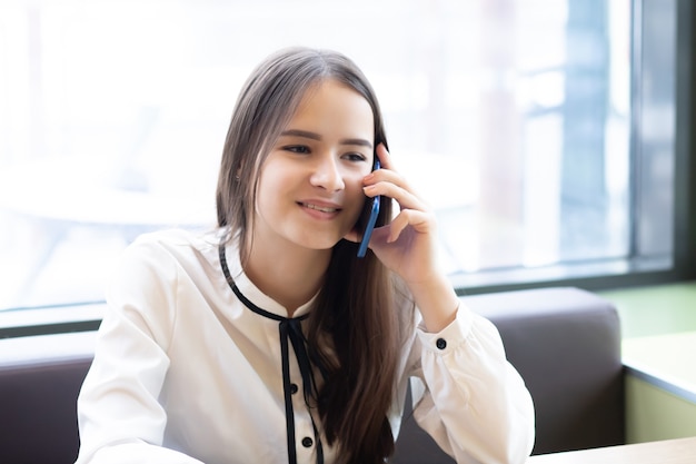 Studentin in einem Café mit einem Smartphone, sprechend, lächelnd