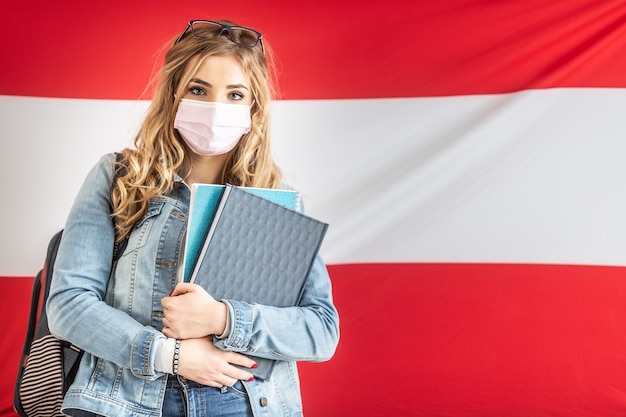 Studentin in Gesichtsmaske steht vor österreichischer Flagge.