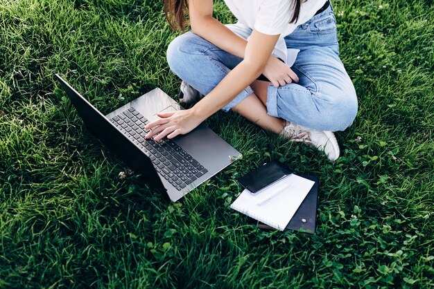 Studentin mit einem Laptop im Freien sitzt auf dem Rasen im Park