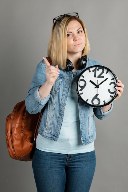 Studentin mit einer großen Uhr in den Händen auf grauem Hintergrund