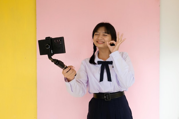 Studentin mit Handy und Selfie-Stick auf rosa Hintergrund