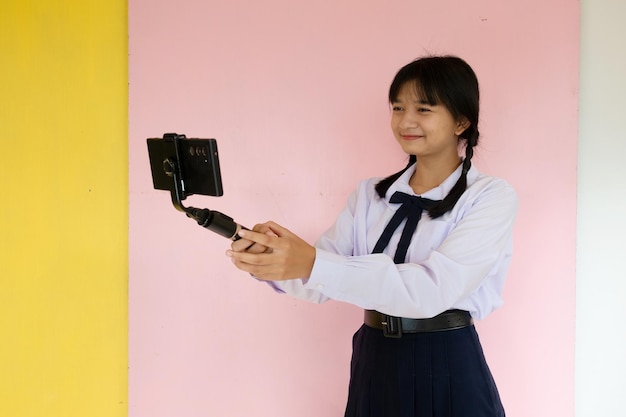 Studentin mit Handy und Selfie-Stick auf rosa Hintergrund