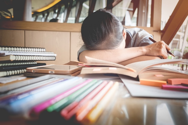 Studentin schläft am Schreibtisch mit Haufen Bücher. Müde vom Studieren.