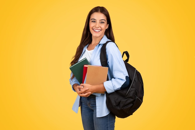 Studentin studiert aufmerksam, umgeben von Büchern vor einem leuchtend gelben Hintergrund