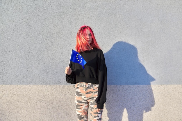 Studentin Teenager mit EU-Flagge in der Hand, grauer Außenwandhintergrund. Europäische Union, Bildungsleben In Europa, Patriotismus-Menschen-Konzept