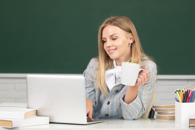 Studentin trinkt Kaffee oder Tee und arbeitet an einem Laptop im Klassenzimmer, um sich auf eine Prüfung vorzubereiten