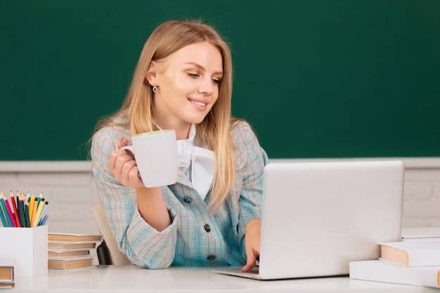 Studentin trinkt Kaffee oder Tee und arbeitet an einem Laptop im Klassenzimmer, um sich auf eine Prüfung vorzubereiten