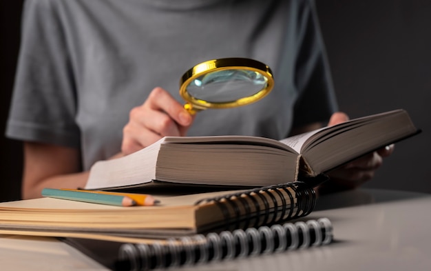 Studentinnen Hände schließen, halten Lupe und Buch oder Lehrbuch, suchen nach Informationen und lesen in der Nacht.