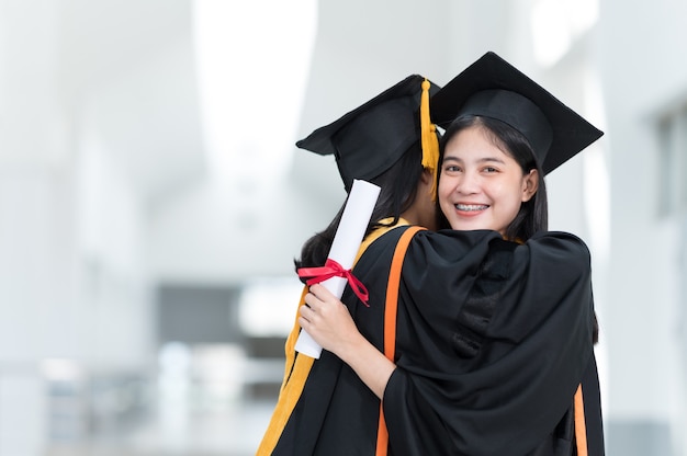 Studentinnen, Universitätsabsolventen, die schwarze Hüte und gelbe Quasten tragen und Freunde glücklich umarmen.