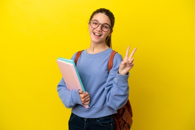 Studentische Kinderfrau über isoliertem gelbem Hintergrund, die lächelt und Victory-Zeichen zeigt