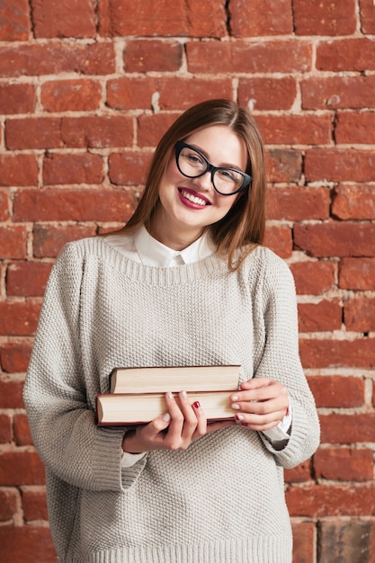 Studentisches Mädchen, das spielerisch mit Büchern lächelt