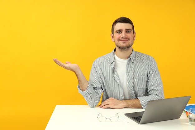 Studienkonzept mit dem jungen Mann, der auf dem Tisch auf gelbem Hintergrund sitzt.