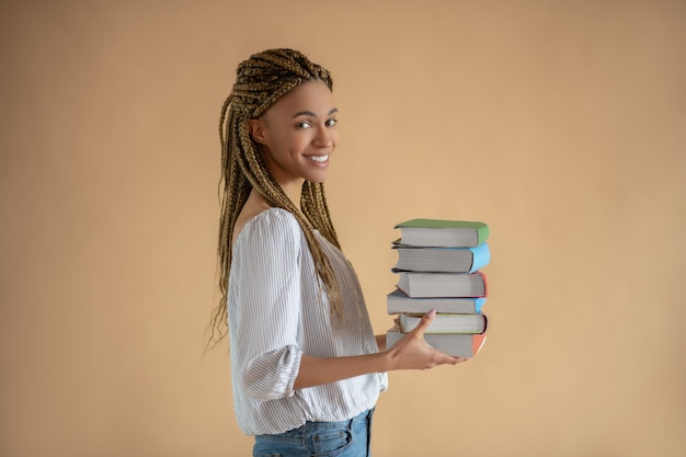 Studienprozess. glückliche junge afroamerikanische frau, die stapel bücher vor ihr trägt