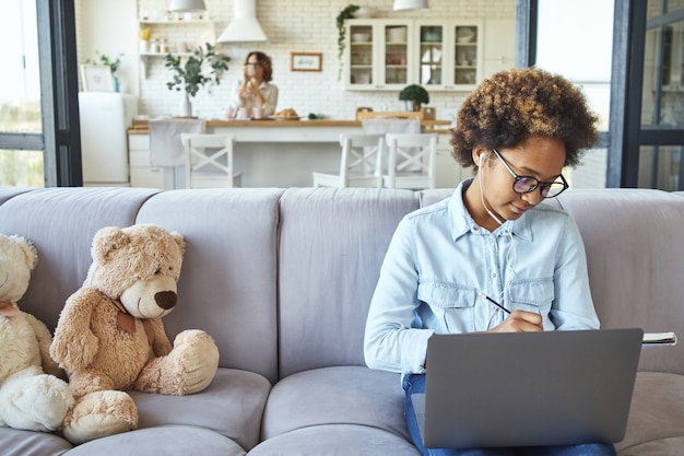 Studieren Sie Ihr eigenes süßes Teenager-Mädchen, das Kopfhörer mit Laptop trägt und Notizen in ihrem Notizbuch macht