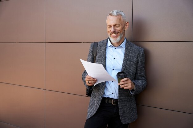 Studieren von Informationen selbstbewusster, stilvoller Geschäftsmann mittleren Alters, der lächelt, während er mit Papieren arbeitet