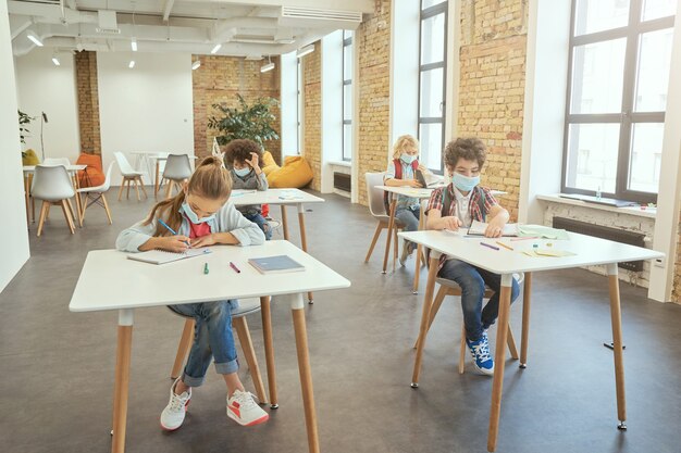 Foto studieren während der pandemie schulmädchen mit gesichtsmaske, die in ihr notizbuch schreibt, während sie an der sitzt